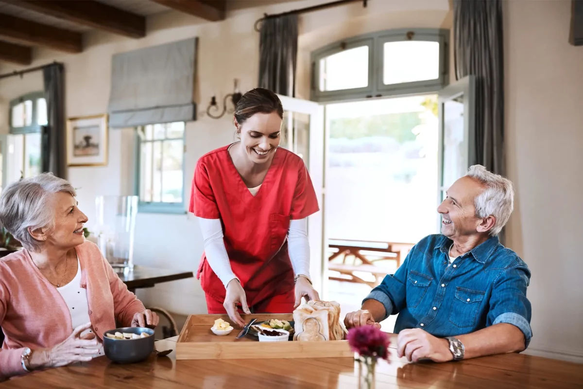 Une auxiliaire de vie servant le petit déjeuner à un couple
